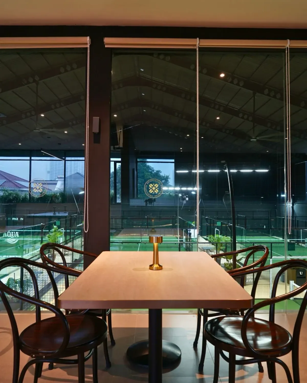 Wooden tables facing the padel court through a glass wall